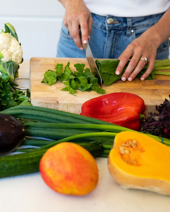 A woman skillfully cuts fresh vegetables on a cutting board, promoting healthy eating with expert dietitian guidance.