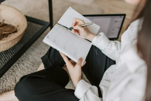 A woman sits on the floor, writing in a notebook, focusing on building healthy nutrition habits and lifestyle changes.