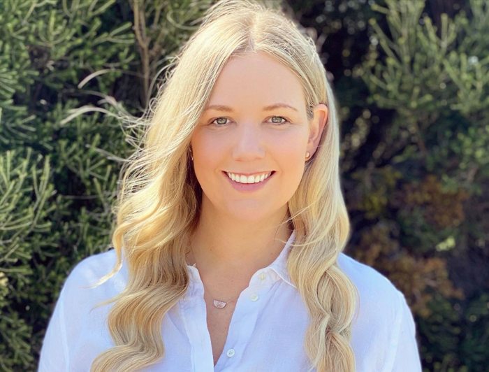 A blonde woman dressed in a white shirt and jeans, symbolizing knowledge in nutrition and women's health topics.